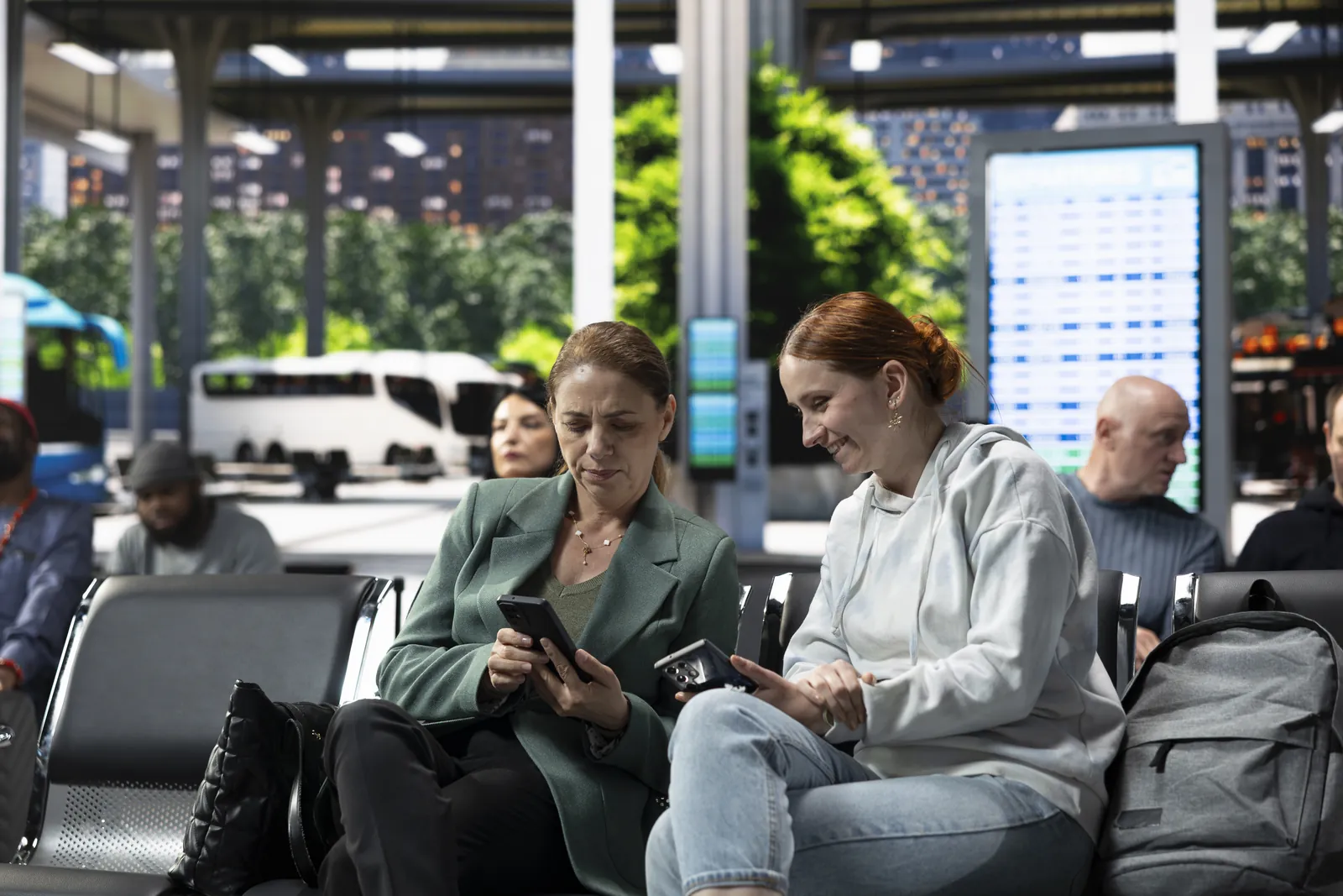 Dos pasajeras revisando sus teléfonos en la sala de espera de una terminal de transporte